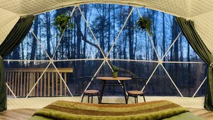 Una tienda de campaña acogedora con una mesa redonda y sillas, ventanas grandes y vistas a un bosque.