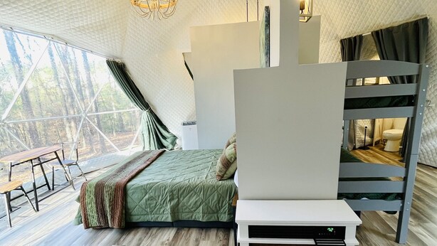 Un dormitorio acogedor con cama, chimenea y ventana grande con vistas a un bosque.