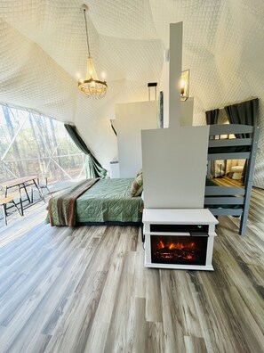 Un dormitorio acogedor con cama, chimenea y ventana grande con vistas a un bosque.