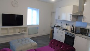 Ein kompakter Wohnbereich mit Flachbildfernseher, einer Couch, einer Küchenzeile mit modernen Geräten und einem Fenster für natürliches Licht.