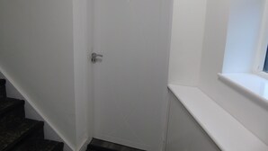 Eine weiße Tür mit einem Zahlen-Schlüsselschloss, oberhalb ein kleines Fenster und eine dunkle Treppe zur Linke.