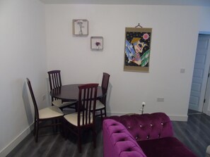 Un comedor con una mesa redonda y cuatro sillas, un sofá púrpura y dos cuadros en la pared.