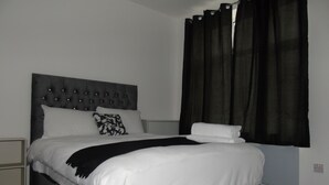 Ein ordentlich bezogenes Bett mit einer karossierten Kopfteile, weißer Bettwäsche und einer schwarzen Decke.