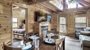 A cozy log cabin interior with a dining area, a fireplace, and a television mounted above it. - Hideaway Hangout! Family Retreat! Beautiful views, 3 decks, hot tub, multicade! (Sevierville)