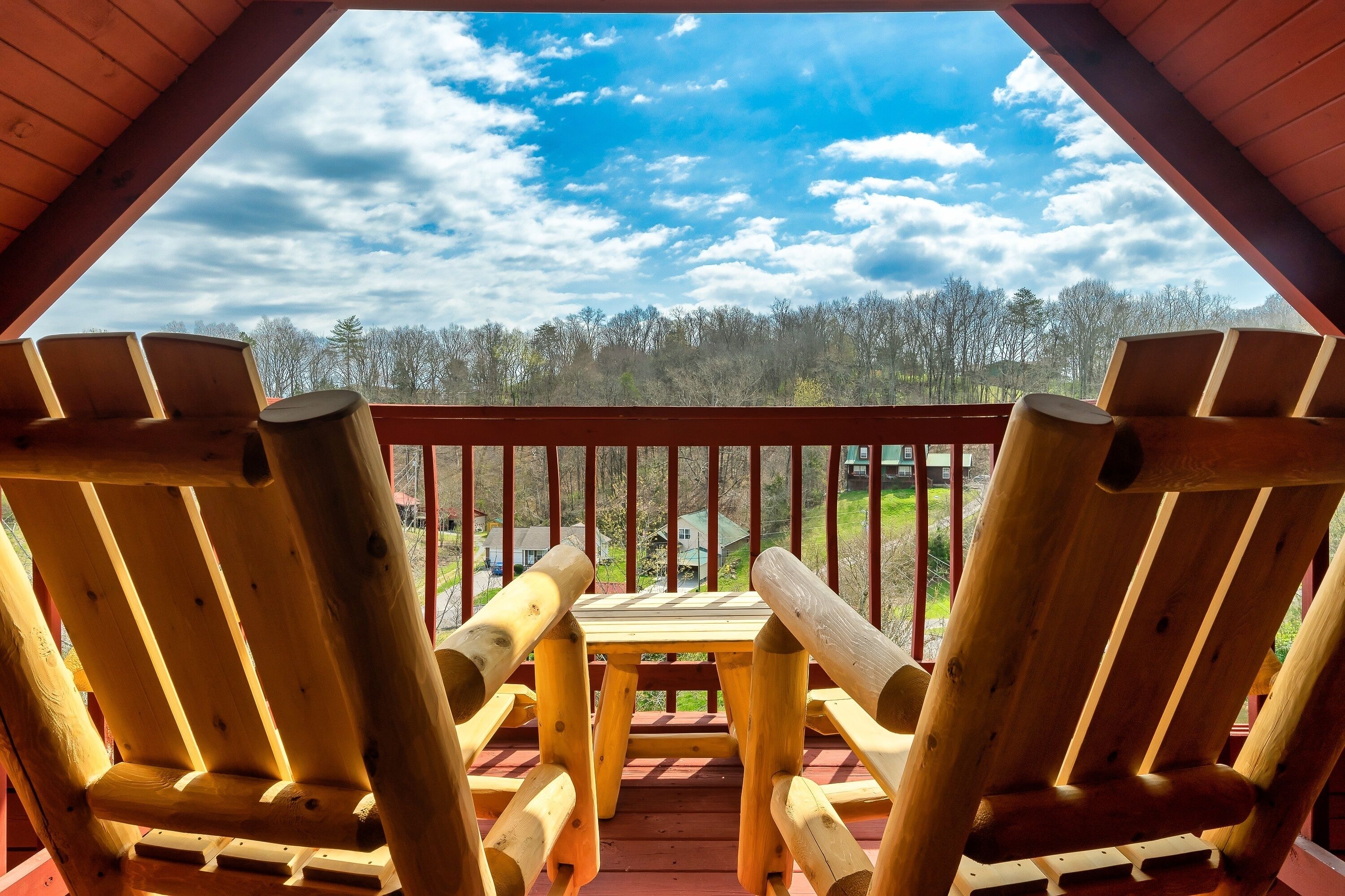 A wooden deck with two Adirondack chairs and a table, overlooking a forested area.