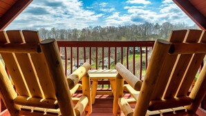 A wooden deck with two Adirondack chairs and a table, overlooking a forested area. - Hideaway Hangout! Family Retreat! Beautiful views, 3 decks, hot tub, multicade! (Sevierville)