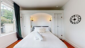 Ein Schlafzimmer mit einem großen Bett, zwei Türen, einem Fenster mit Vorhängen und einer Wanduhr.