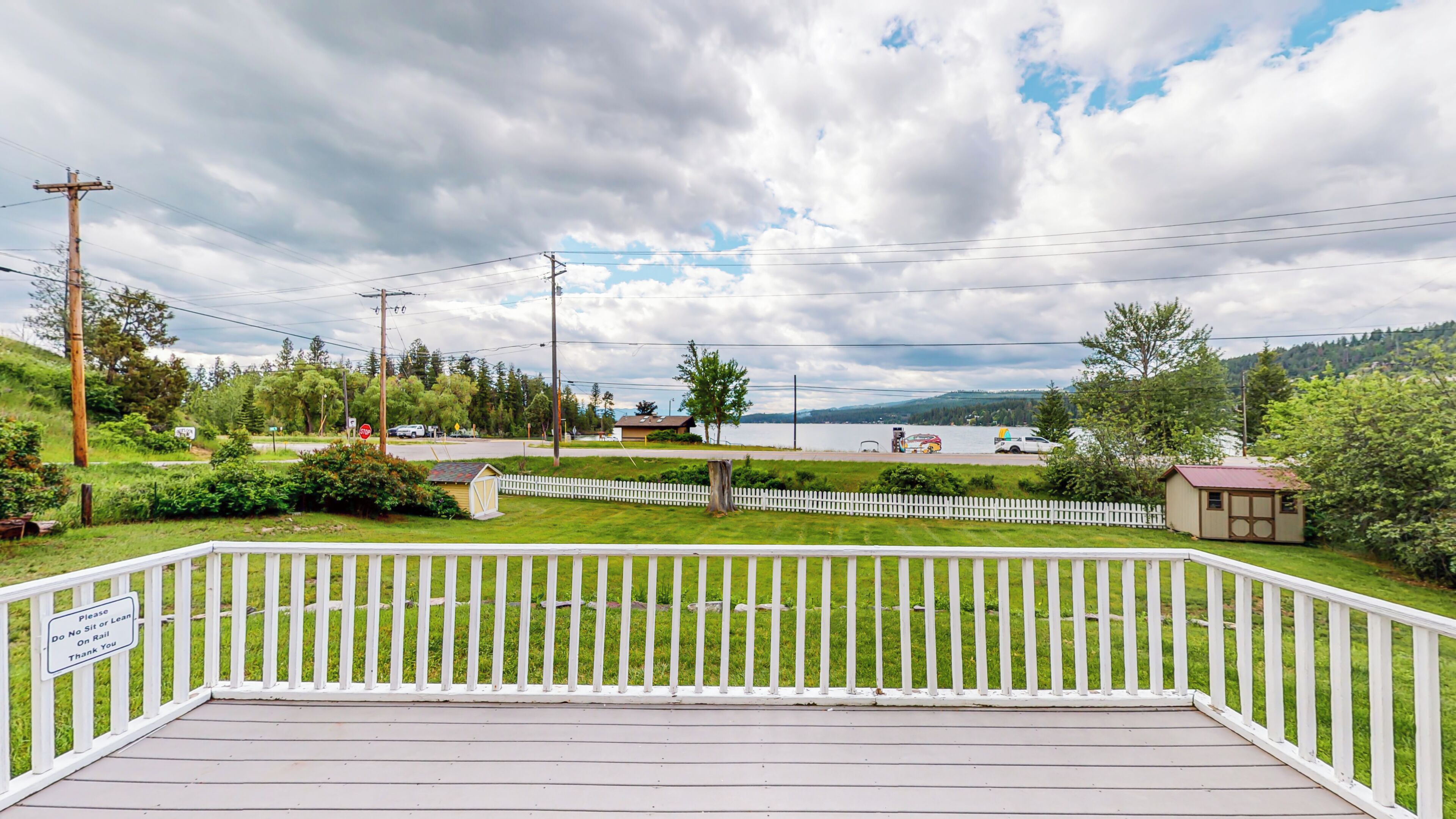 A deck with a white railing, a small shed, and a sign prohibiting sitting or leaning on the rail.