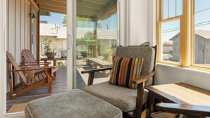 Une pièce avec une terrasse en bois, un fauteuil rembourré agrémenté d’un coussin à rayures et une table en bois.