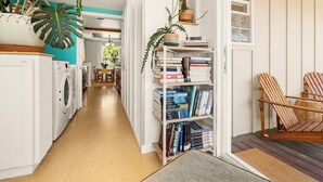 Un espace buanderie avec un lave-linge et un sèche-linge, une bibliothèque remplie de livres et de plantes, et une chaise en bois.
