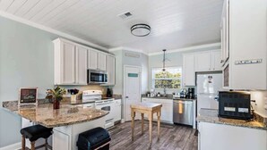 A kitchen with white cabinets, granite countertops, a microwave, stove, refrigerator, and a window with a view of greenery. - Our Place On 30a (Santa Rosa)