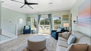 A spacious living room with a ceiling fan, a large window with curtains, a blue sofa, a beige sofa, and a round ottoman. - Our Place On 30a (Santa Rosa)