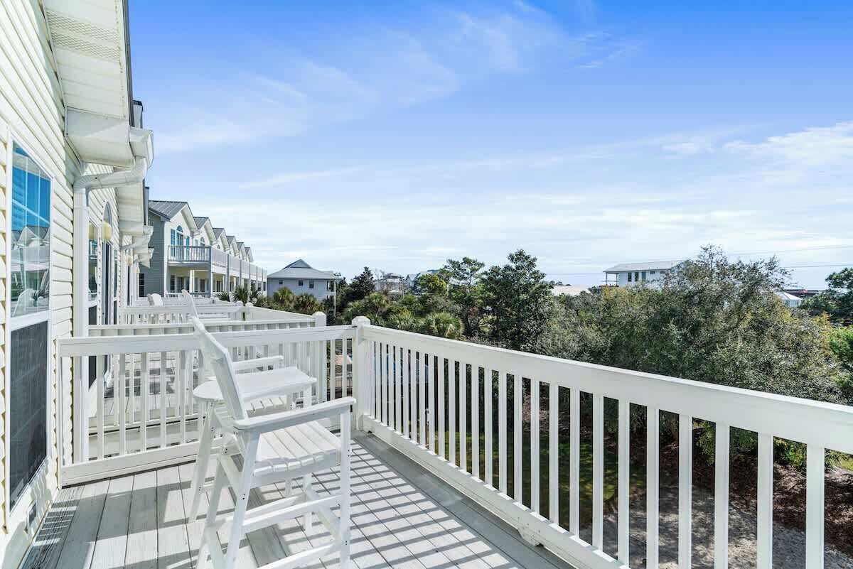 A wooden deck with white railings and a white chair, overlooking a residential area with houses and trees.