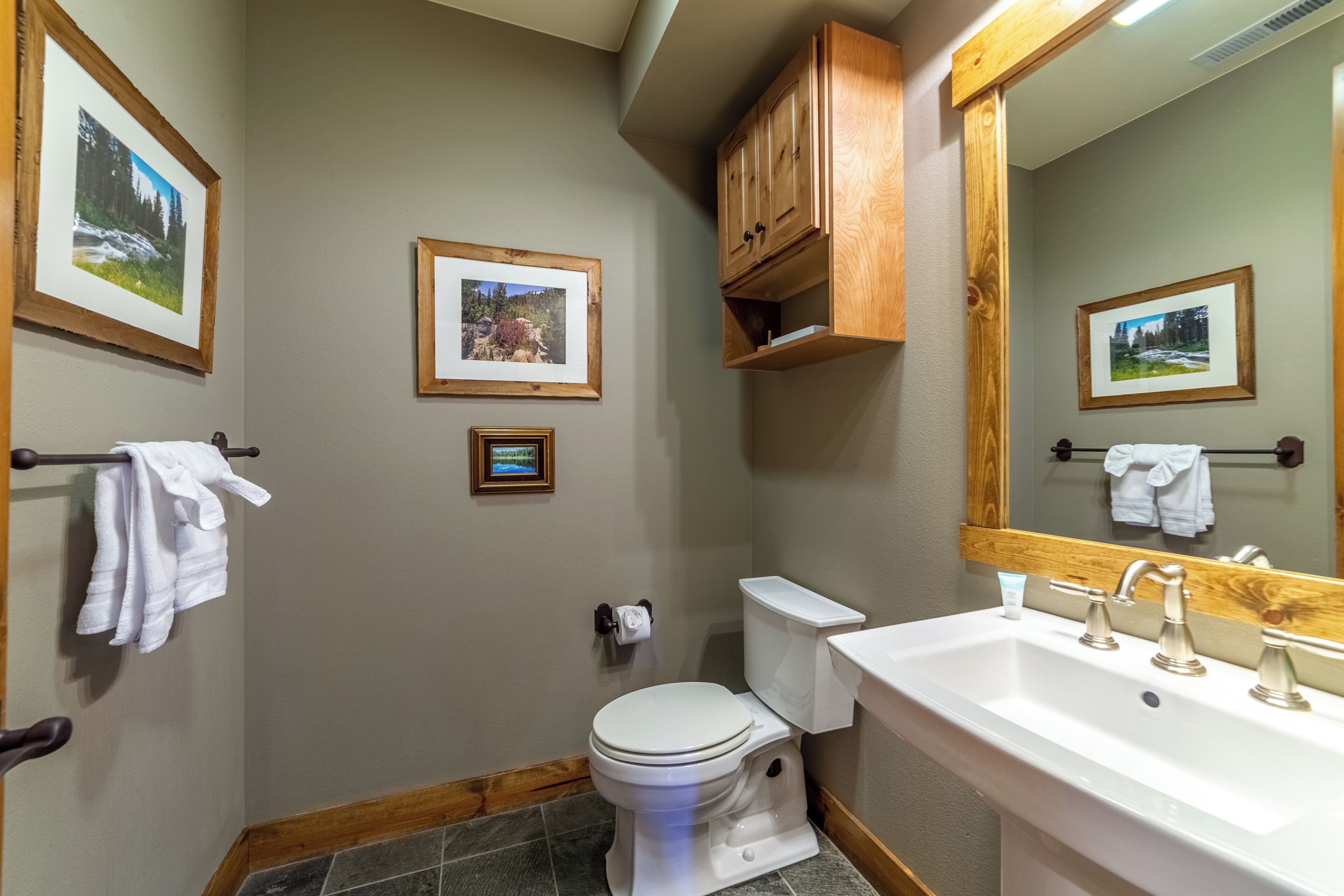 Une salle de bain avec des toilettes, un lavabo et un meuble en bois. Des tableaux encadrés ornent les murs.
