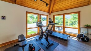 Et fitnesscenter med træningsudstyr, store vinduer og et træloft.