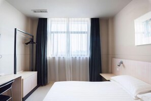 A hotel room with a bed, a desk, a chair, a wardrobe, and a window with curtains. - Jinjiang (Gaoyou Haichao East Road) (Gaoyou)