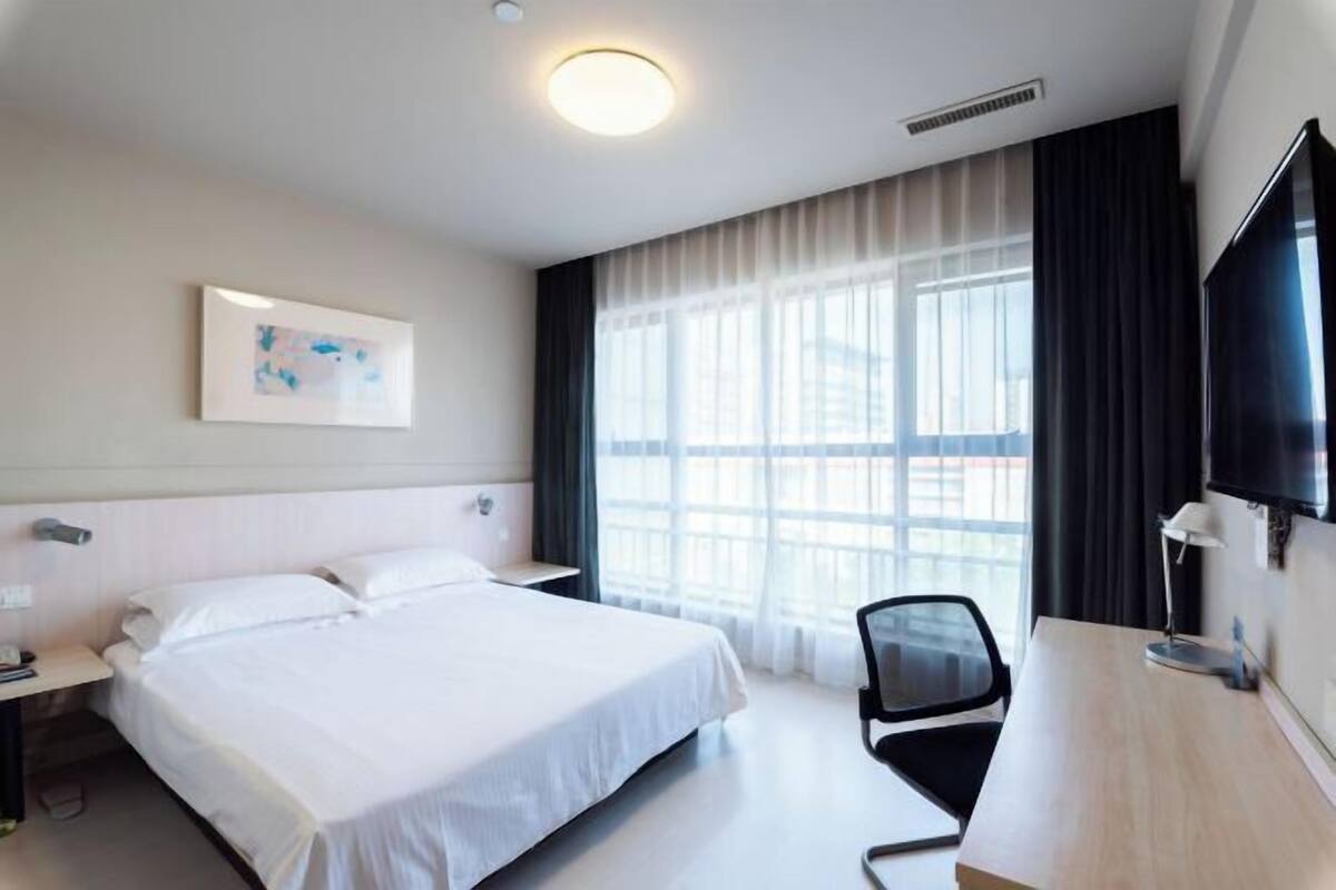 Habitació d'hotel amb llit, escriptori, cadira, televisió i finestra amb cortines.