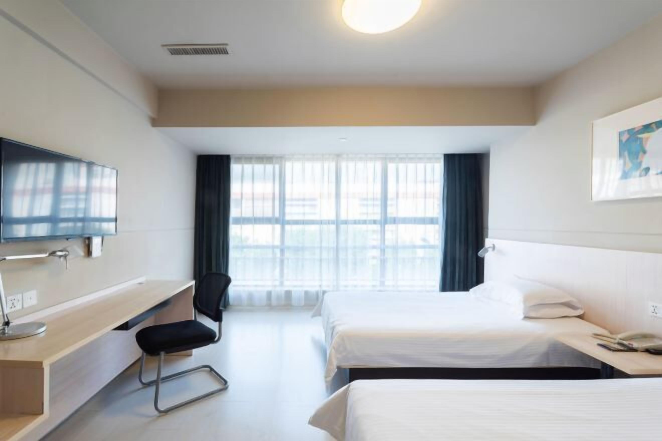 Una habitación de hotel con cama, un escritorio con silla, televisión y ventana con cortinas.