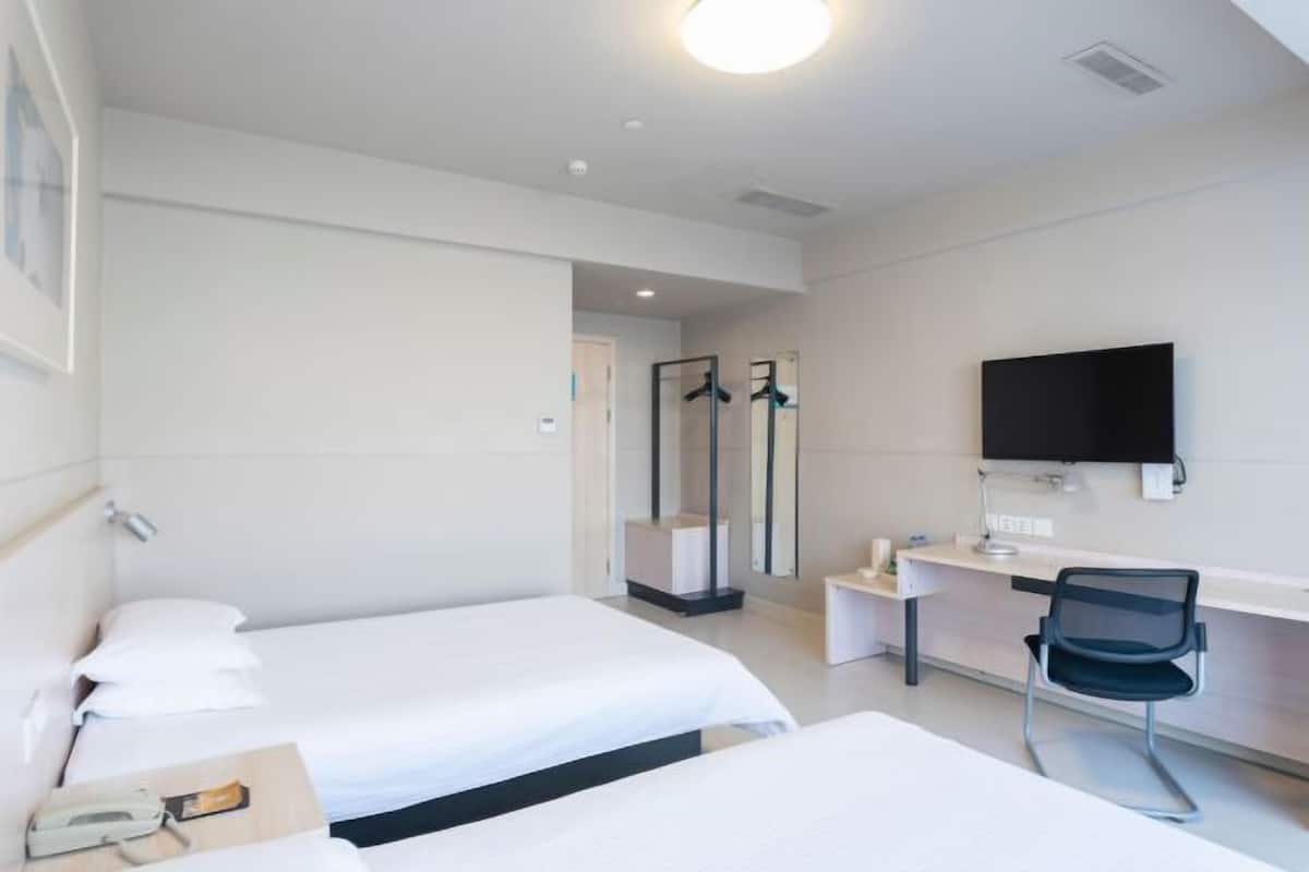 Habitació d'hotel amb dos llits, un escriptori, una cadira, un televisor i un mirall.
