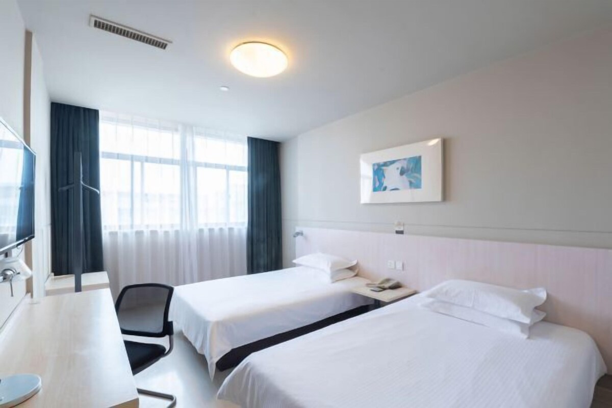 A hotel room with two beds, a desk, a chair, a TV, and a window with curtains.