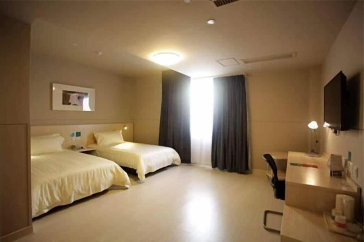 Habitació d'hotel amb dos llits, una taula de treball amb una cadira, televisió i finestra amb cortines.
