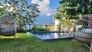 Ein rechteckiger Pool mit Glasboden, umgeben von Gras, mit je zwei Korbstühlen an den Seiten.
