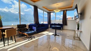 Ein modernes Wohnzimmer mit großem Fenster und Bergblick, einer Couch, einem Essbereich und einem kleinen Tisch.