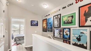 A hallway with a reception desk, framed movie posters on the wall, and a bed in the background.