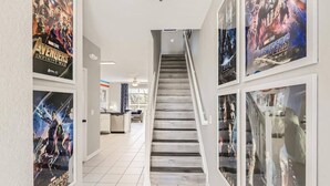 A hallway with a staircase, posters of Avengers movies, and a kitchen area in the background.