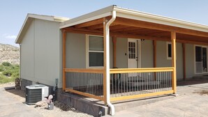 Een overdekt terras met houten balustrade, een deur en een raam.