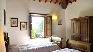Une chambre avec deux lits, une fenêtre donnant sur un paysage verdoyant, des meubles en bois et des tableaux accrochés au mur.