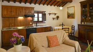 A cozy kitchen with wooden cabinets, a dining area with a table and chairs, and a sofa with a cushion. - San Pietro Geranio - Apartment with swimming pool (Cortona)