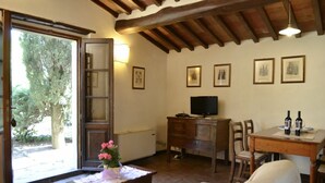 Un salon chaleureux avec un plafond en bois, un téléviseur, une table à manger ornée de bouteilles de vin et une porte donnant sur un jardin.
