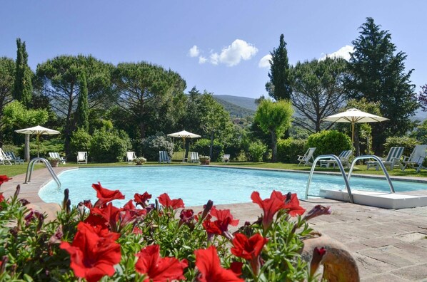 Una piscina con tumbonas y sombrillas, rodeada de árboles y flores.