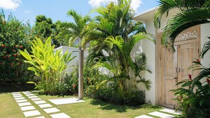A tropical garden with a paved walkway leading to a wooden door. - Villa Aloui by Villa Finder (Kerobokan)