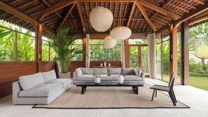A spacious living room with a high ceiling, large windows, and a view of lush greenery. - Villa Aloui by Villa Finder (Kerobokan)
