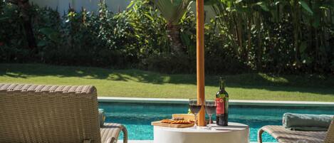 A poolside setting with wicker chairs, a table with a bottle of wine and a glass, and a pool in the background.