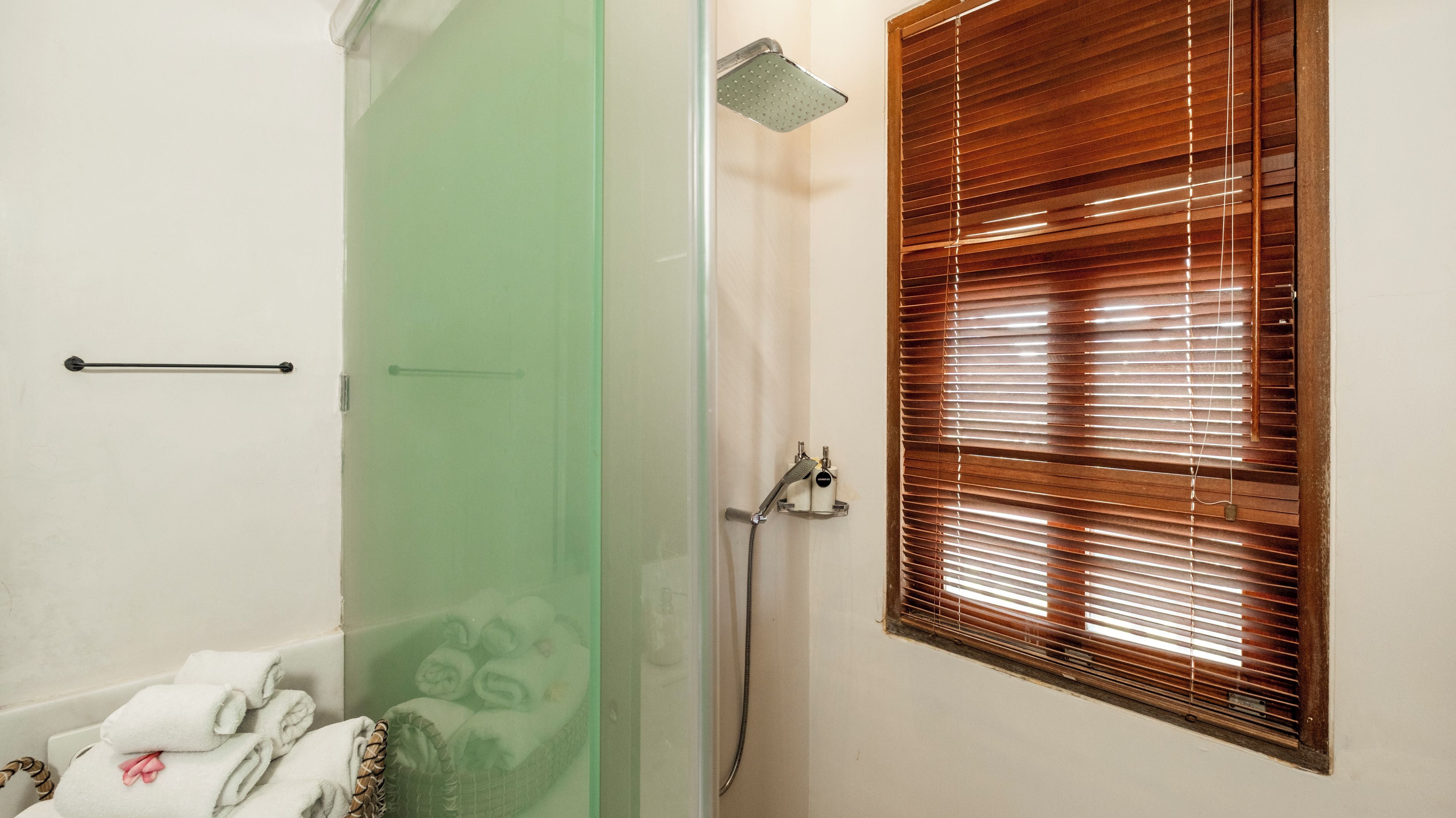 Une salle de bain avec une douche, un porte-serviettes et une fenêtre avec des stores.