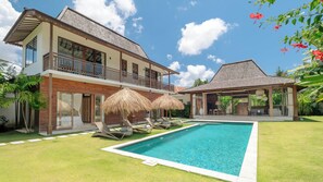 Uma casa de dois andares com piscina, varanda coberta e um jardim exuberante.