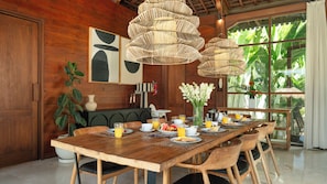 Una mesa de madera con sillas, rodeada por un ventanal con vista a follaje.
