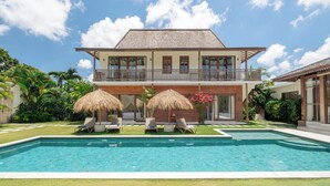 A two-story house with a swimming pool, a balcony, and a garden with lounge chairs and umbrellas. - Villa Aloui by Villa Finder (Kerobokan)