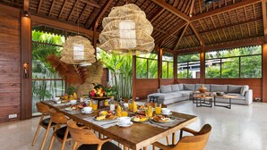 A spacious dining area with a wooden table set for breakfast, surrounded by chairs with black cushions. - Villa Aloui by Villa Finder (Kerobokan)