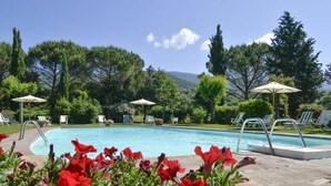Ein Pool mit Liegestühlen und Sonnenschirmen, umgeben von Bäumen und Blumen.