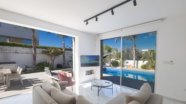 A modern living room with a large sofa, a dining area, and a view of a swimming pool.