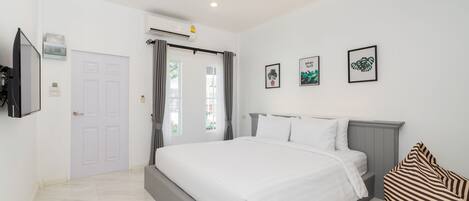 A modern bedroom with a large bed, a flat-screen TV mounted on the wall, and a window with curtains.