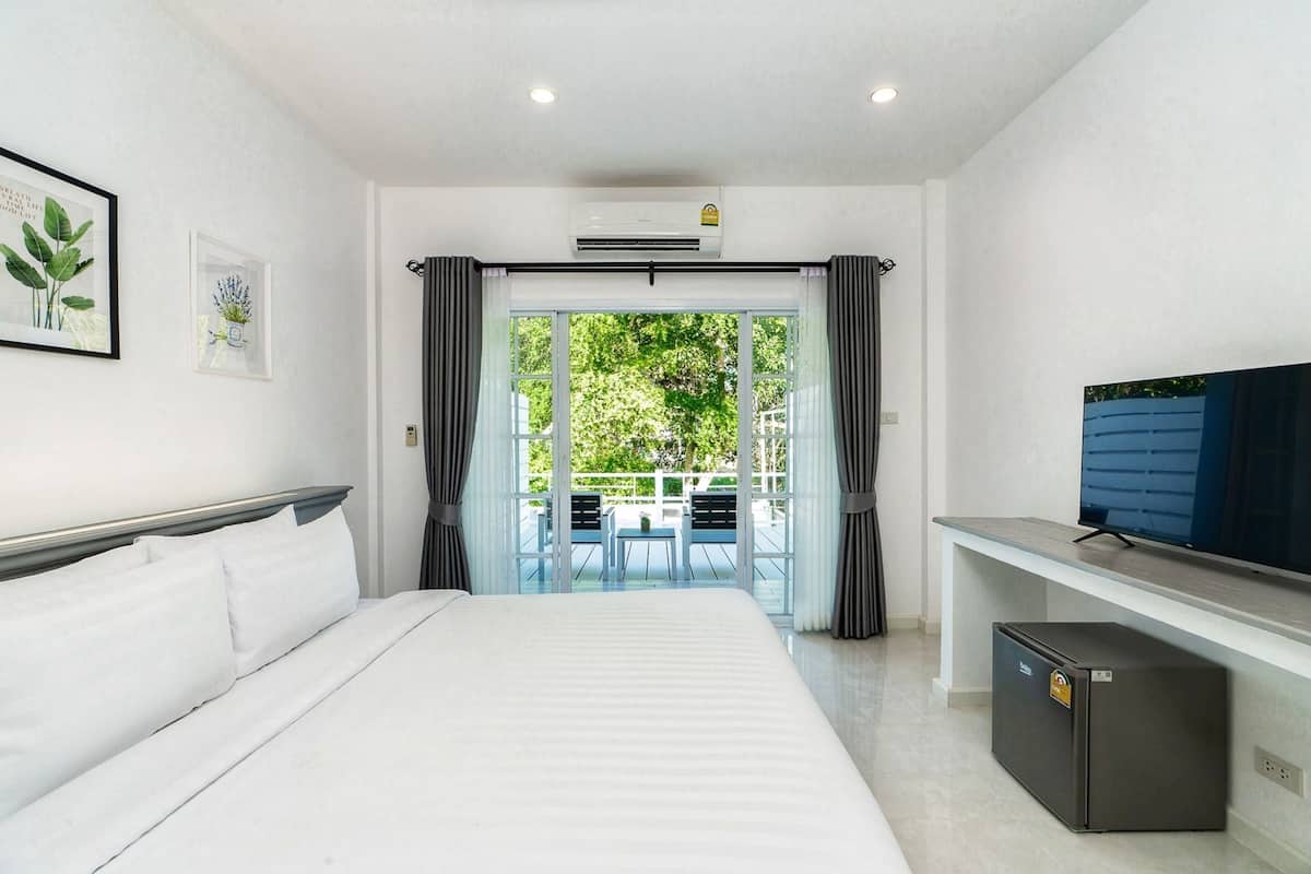 Ein Hotelzimmer mit Bett, Fernseher, kleinem Kühlschrank und einem Balkon mit Tisch und Stühlen.