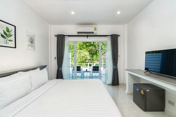 Habitación de hotel con cama, televisión, refrigerador pequeño y balcón con mesa y sillas.