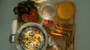 Comida con una olla de guiso, tomates en rodajas, lechuga, pan y salsas sobre una tabla de madera.