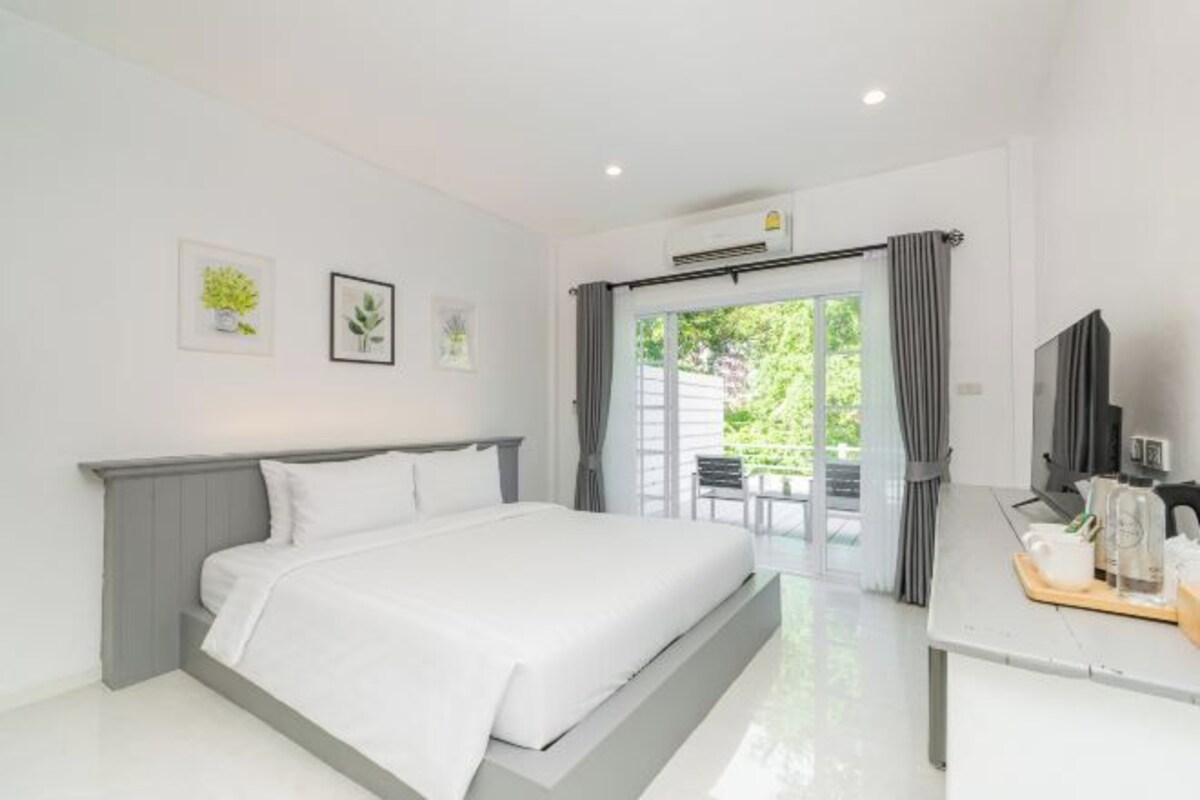 A modern bedroom with a large bed, a desk with a chair, and a view of greenery outside.