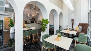Un interior moderno con zona de comedor, sillas verdes, un sofá y una cocina al fondo.